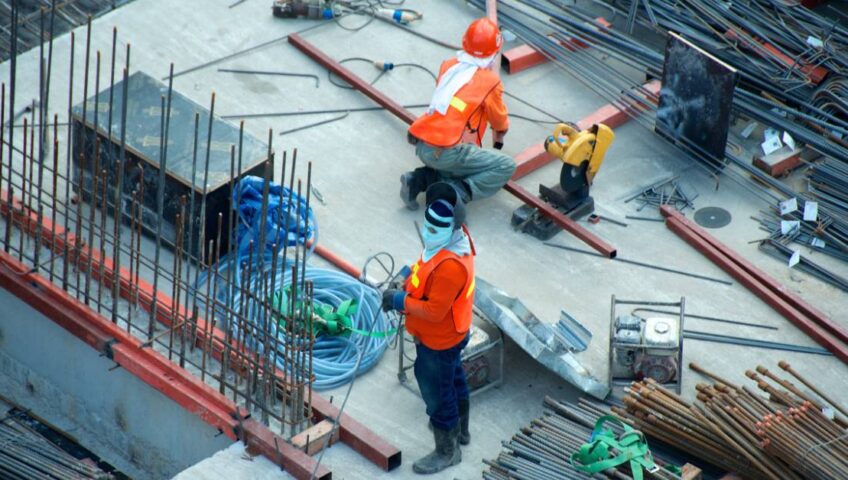 Two men in safety vests working on a construction site with steel rods